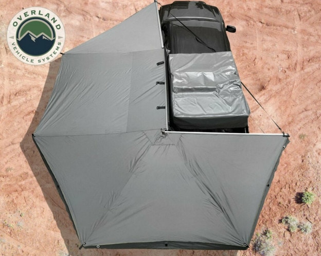 A birds-eye view of a black overlanding vehicle on sandy ground with the OVS 270-degree grey awning set up around it.
