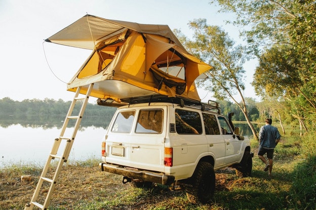 Soft shelled roof top tent on white Jeep near lake