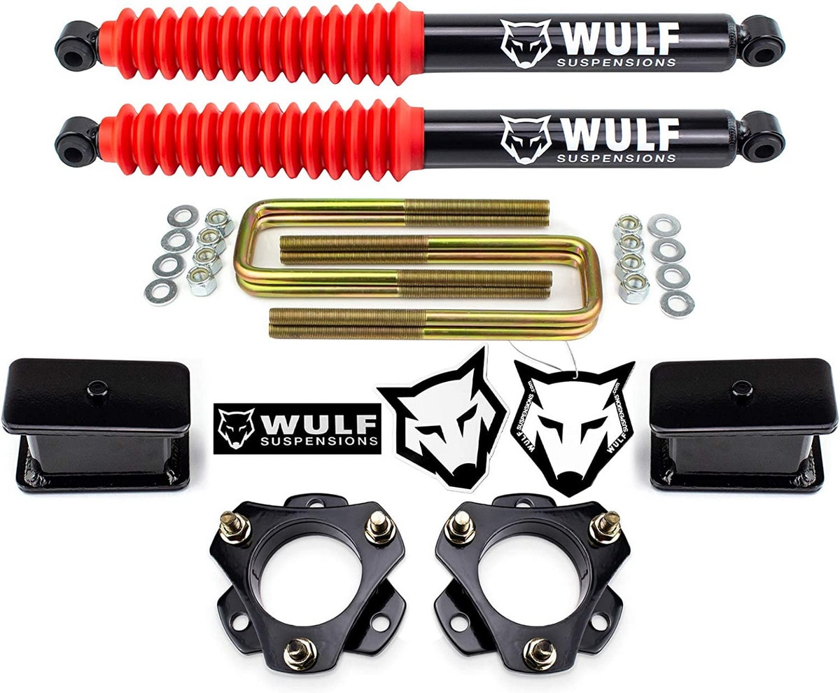 Two strut spacers, two angled blocks, four U-bolts, two WULF Shock Absorbers, and two red shock dust boots all lie evenly spaced on a white background.