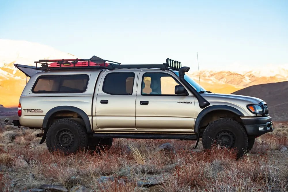 a budget overland Tacoma build parked in a field with mountains in the background